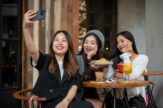 Group of attractive Asian female friends are taking selfies while hanging out at a cafe together.