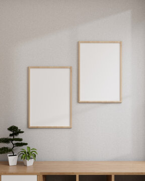Minimal white room with blank picture frames mockup hanging on a white wall above a wooden bookcase.