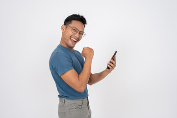 An excited Asian man is holding his phone and showing his triumph gesture, isolated background.