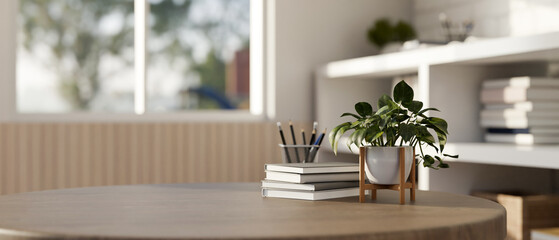 An empty space on a hardwood table with a potted plant, books, and a pencil stand in a modern room.