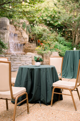 A table is set up outside by a waterfall with green tablecloth and chairs surrounding it. 