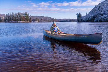 young woman paddling a green canoe solo on a river with trees clad in freshly fallen snow in the...