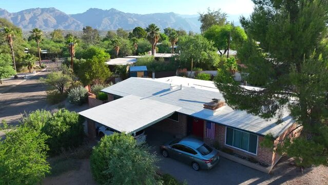 Southwest USA home with American flag. Aerial view of house in neighborhood with green palm trees and mountain background.