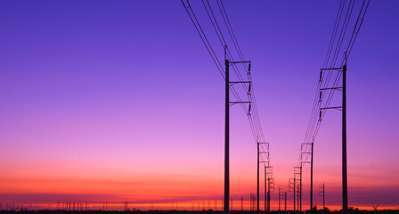 Silhouette row of electric poles with cable lines on curve road in industrial settlement area...