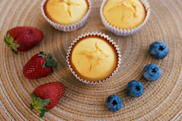 Fototapeta na wymiar Top view closeup shot of delicious tasty homemade baking cupcakes placed on wooden weave rattan table decorating with organic fresh raw strawberry blackberry in kitchen