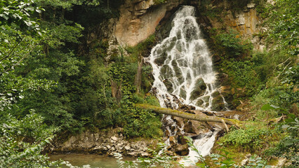 Amazing waterfall, water cascading down the cliff. Green forest around. Summer. Water flowing into...