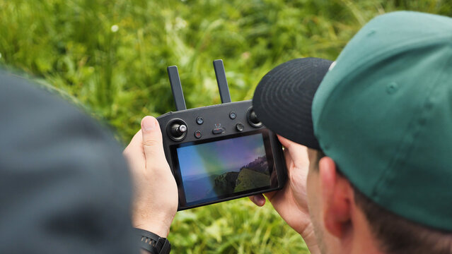 Close-up of drone pilot's hands controlling the quadrocopter remote control while moving. View of hands and screen. The screen shows the image from the camera of the UAV drone.