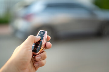 The driver hand is holding a keyless key to unlocking the car, photo with  luxury car as blurred background. Ready for driving concept scene.