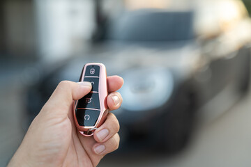 The driver hand is holding a keyless key to unlocking the car, photo with  luxury car as blurred background. Ready for driving concept scene.