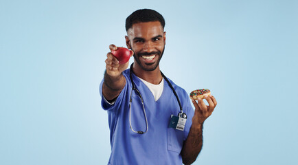 Happy man, doctor and apple with donut for diet or healthy eating by a blue studio background. Portrait of male person or medical nurse smile with organic fruit and chocolate dessert for choice - obrazy, fototapety, plakaty