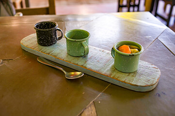 A wooden board in a cafe with three cups with vegetables and salsas on table with spoon in a cafe in Mexico.