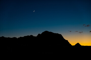 Silhouette of mountains at dusk and a crescent moon