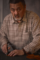 serious bearded craftsman working with leather using crafting DIY tools, loosing at the camera, sitting at the table at workshop, lifestyle