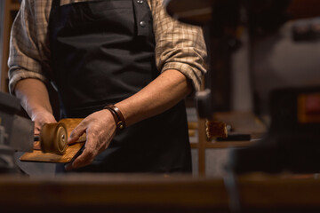 focus on craftsman's hand holding piece of cloth, standing behind leather edge grinding machine. close up cropped photo - obrazy, fototapety, plakaty