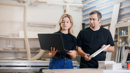 Designer with laptop approves wooden furniture project with carpenter in workshop. DIY Industrial...