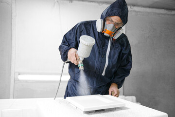Application white color on facade kitchen furniture, spraying device. Painter staining wood with...