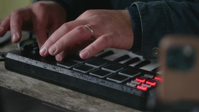 Close up of male musician playing digital electric piano and composing music, sitting outdoors in forest. Caucasian man uses laptop and phone on tripod to record song on his vacation in mountains.