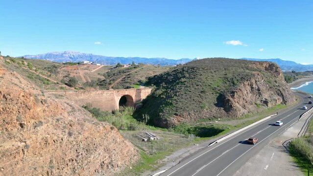 Old bridge on coast road in Southern Spain with views over the mountains with clear visibility on bright sunny day.