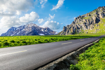 Asphalt highway and green meadows with mountain natural landscape under the blue sky