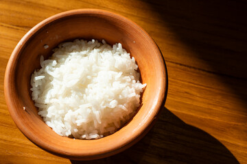 Rice in clay pot on wooden table with sun light.