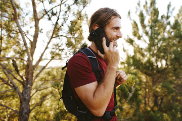 Male hiker with a backpack is talking on the phone in the countryside