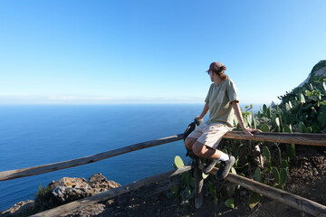 Young man Daylight Contemplation: Solo Traveler Admiring Expansive Ocean View from Mountain Top, in Wide-Angle