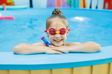 A little girl of 7 years swims in the pool. The girl is sitting in the pool in swimming goggles.