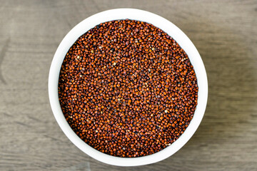 Red quinoa on the white plate on the wooden background. Healthy food and nutrition concept. Safe, ecological, and healthy products