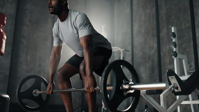 Man do deadlift with barbell in hands. African american guy exercising making squats holding heavy barbell in gym. Sport powerlifting training workout healthy lifestyle make athletic body concept.