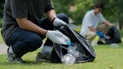Man's hand collecting plastic waste bottles into a black bag in a park.Ecology concept.Social...