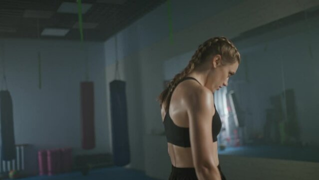 Slow motion, portrait of a woman pro fighter standing in a boxing gym and looking into the camera, tired woman, soft focus.