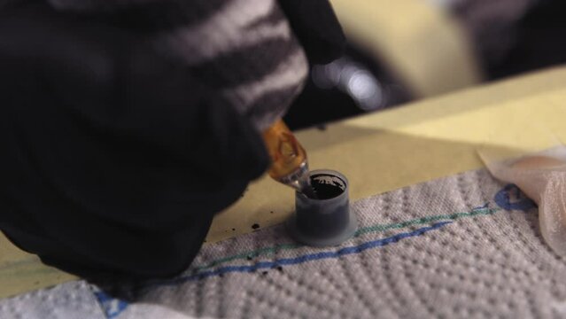 Slow motion footage of a tattoo gun's needle being dipped into a small container of black ink.