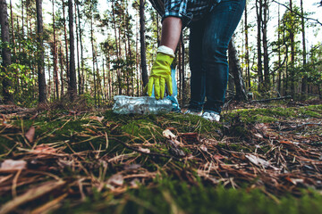 A plastic bottle lies on the moss in the sun. In the forest, a woman volunteer came up with a garbage bag to pick up plastic waste. Pollution of the forest with household waste and plastic garbage.