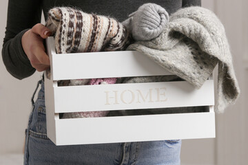 Woman holding wooden box with warm clothing items, donation and charity concept, domestic life, organization and decluttering.