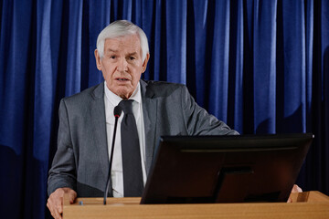 Portrait of mature businessman in suit looking at camera while giving his speech at conference