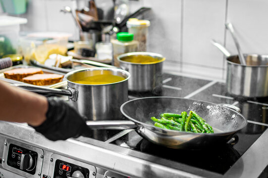 Professional chef cooking asparagus in frying pan on stove in restaurant kitchen