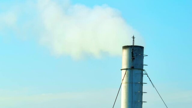 Against a backdrop of blue skies, an industrial plant emits white smoke, illustrating the grave respiratory risks associated with unchecked pollution. Environmental impact and carbon dioxide concept. 