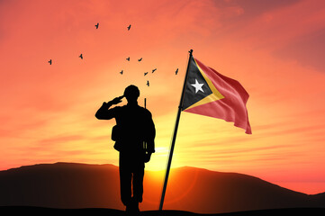 Silhouette of a soldier with the East Timor flag stands against the background of a sunset or sunrise. Concept of national holidays. Commemoration Day.