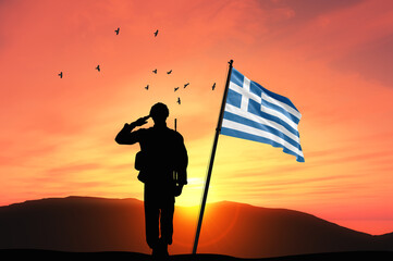 Silhouette of a soldier with the Greece flag stands against the background of a sunset or sunrise....