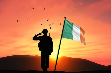 Silhouette of a soldier with the Ireland flag stands against the background of a sunset or sunrise. Concept of national holidays. Commemoration Day.