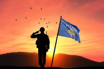 Silhouette of a soldier with the Kosovo flag stands against the background of a sunset or sunrise....