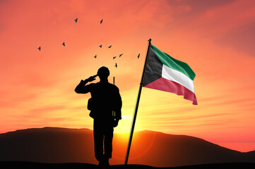 Silhouette of a soldier with the Kuwait flag stands against the background of a sunset or sunrise....