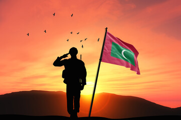 Silhouette of a soldier with the Maldives flag stands against the background of a sunset or...