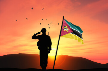 Silhouette of a soldier with the Mozambique flag stands against the background of a sunset or sunrise. Concept of national holidays. Commemoration Day. - obrazy, fototapety, plakaty