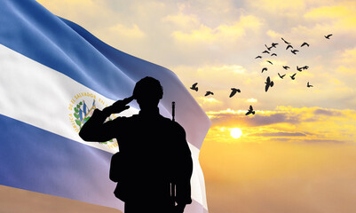 Silhouette of a soldier with the El Salvador flag stands against the background of a sunset or...