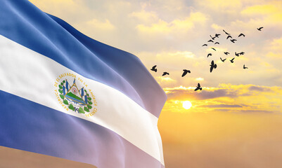 Waving flag of El Salvador against the background of a sunset or sunrise. El Salvador flag for...