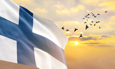 Waving flag of Finland against the background of a sunset or sunrise. Finland flag for Independence Day. The symbol of the state on wavy fabric. - obrazy, fototapety, plakaty