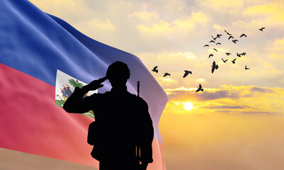 Silhouette of a soldier with the Haiti flag stands against the background of a sunset or sunrise....