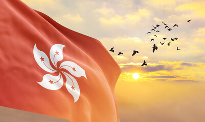 Waving flag of Hong Kong against the background of a sunset or sunrise. Hong Kong flag for Independence Day. The symbol of the state on wavy fabric.