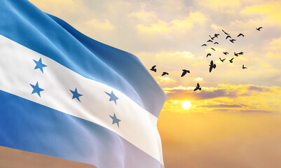 Waving flag of Honduras against the background of a sunset or sunrise. Honduras flag for Independence Day. The symbol of the state on wavy fabric. - obrazy, fototapety, plakaty